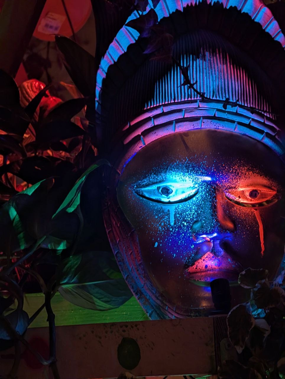 A painted mask glowing under UV light among the leaves